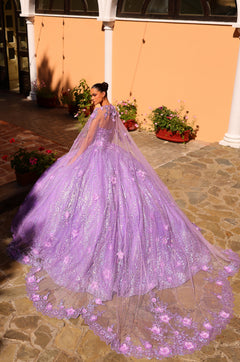 A lavender ball gown with a flowing cape and floral embellishments, worn on a stone patio with potted plants.