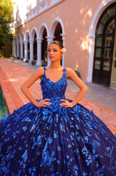 A woman in a royal blue sequined ballgown poses confidently in front of an arched building.