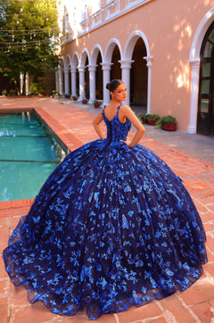 A royal blue quinceañera gown with butterfly details, worn poolside at a Spanish-style venue with white arches.