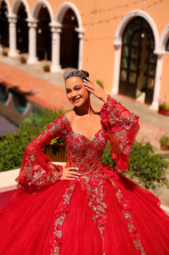 A woman in a vibrant red quinceañera gown with silver embellishments poses elegantly in an arched courtyard.