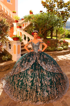 A model wears an emerald green quinceañera gown with intricate silver floral embroidery in a garden setting.