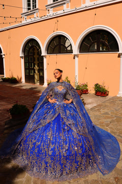 A woman in a Royal Blue/Gold ballgown stands in an arched courtyard with ornate embellishments.
