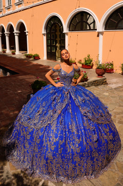 A royal blue quinceañera gown with silver embellishments, worn in a Mediterranean-style courtyard.