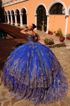 A young woman in a royal blue ball gown with silver embellishments poses dramatically in an arched courtyard.