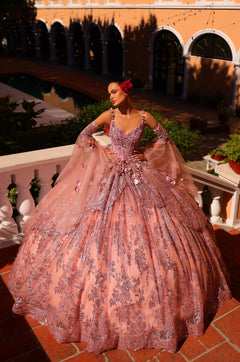 A woman wears a dramatic rose gold ballgown with sparkling embellishments in an elegant courtyard setting.