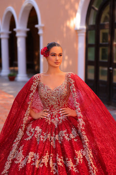 A woman wears an elaborate red ball gown with silver embroidery and a red flower in her hair.