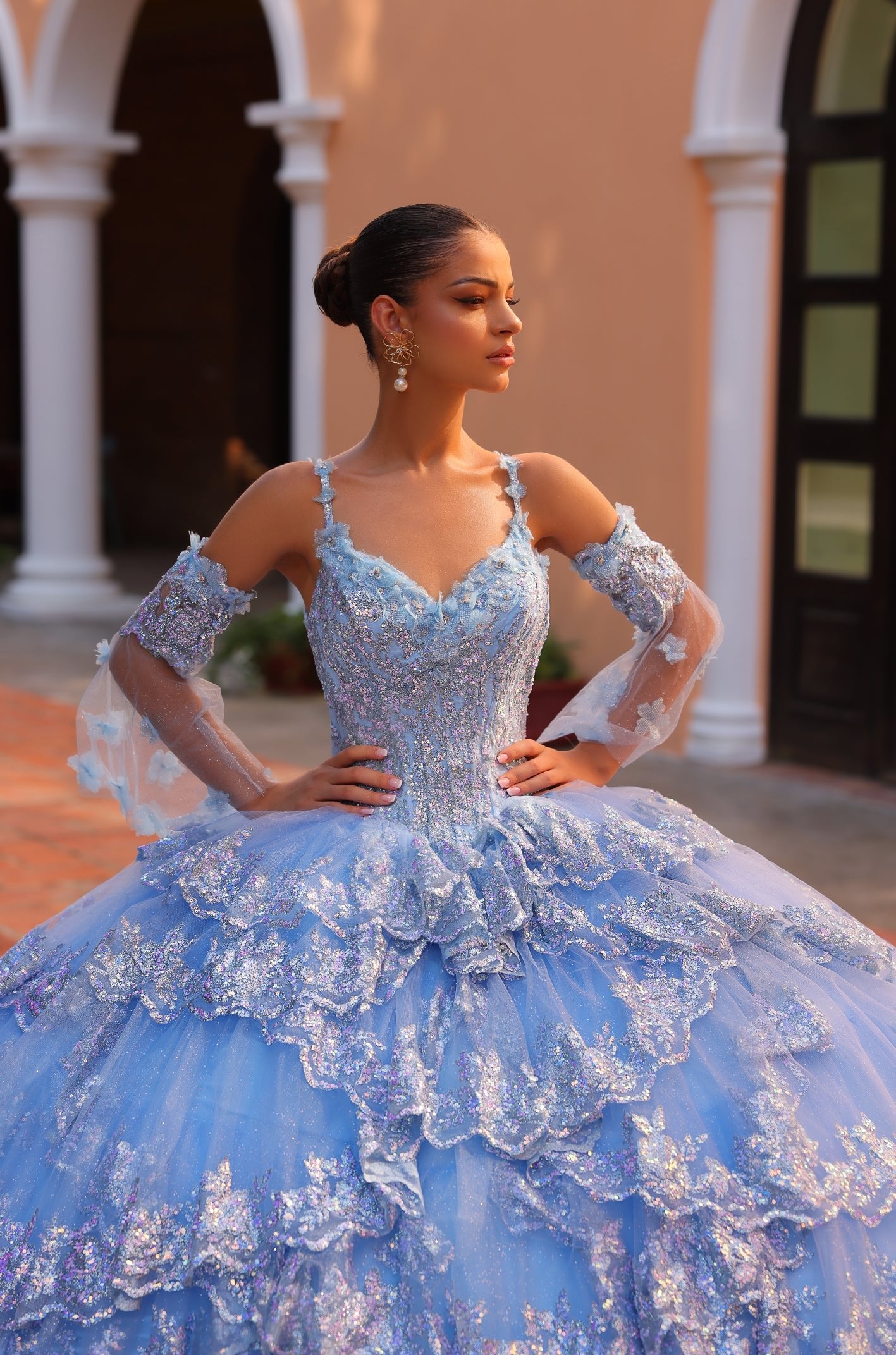A woman in a blue sparkly ball gown poses elegantly with white columns in the background.