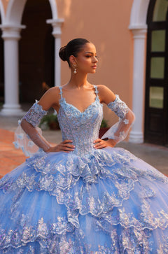 A woman in a blue sparkly ball gown poses elegantly with white columns in the background.