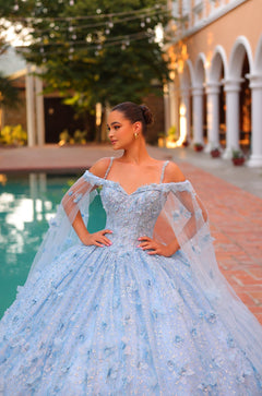 A woman in a sparkling blue ball gown stands by a pool, wearing an off-shoulder dress with delicate tulle details.