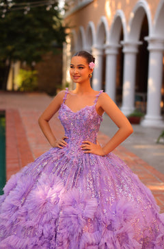 A young woman wears a lavender ball gown with floral embellishments, posing confidently on a brick pathway.