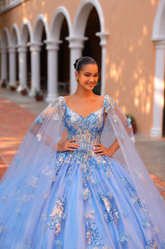 A young woman wears a blue ballgown with shimmering floral details, standing confidently in an arched architectural setting.