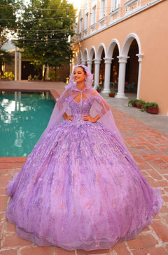 A woman in a lavender ball gown with a matching cape poses by a pool in an elegant courtyard setting.