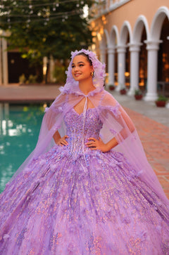 A young woman wears a lavender ballgown with a flowing cape, posing elegantly by a pool.
