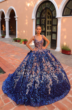 A model wears a Royal Blue/Multi floral ball gown with intricate embellishments on brick-lined architectural grounds.