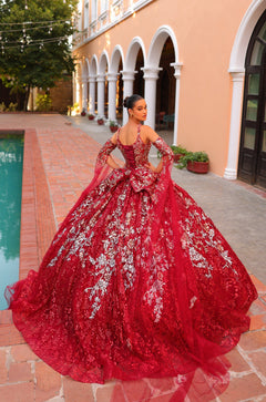 A woman wears an elaborate red and silver quinceañera ball gown with floral embroidery near a poolside venue.