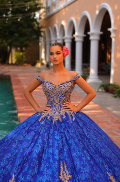 A young woman in a royal blue ball gown with gold embellishments poses confidently in an arched architectural setting.