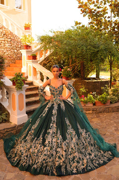 A woman wears an elaborate emerald ball gown with intricate gold lace detailing.