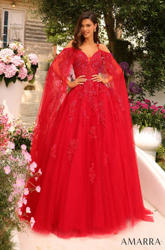 A model wears a vibrant red ball gown with lace details and flowing cape sleeves in a garden setting.