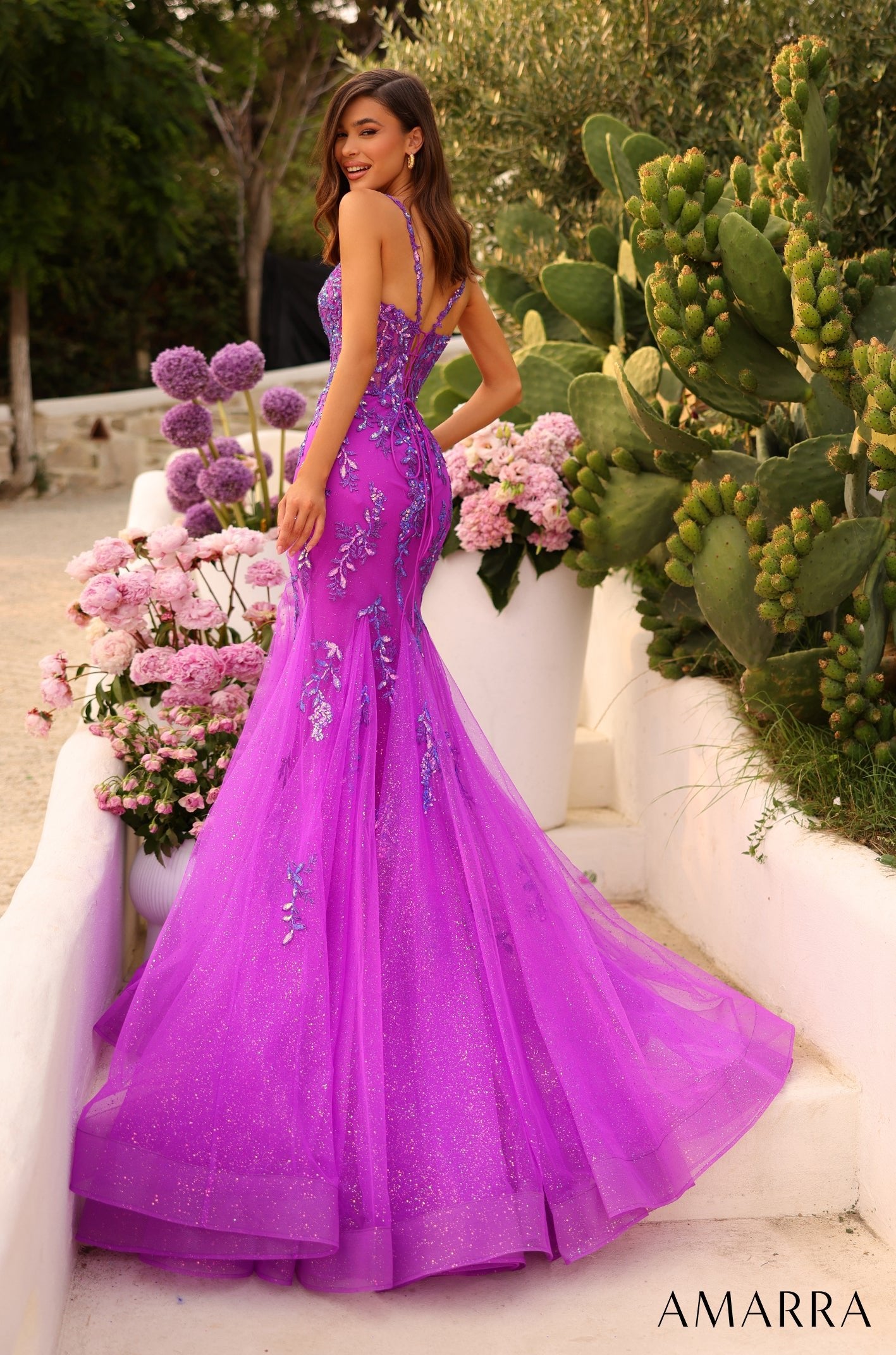 A radiant woman in a purple sparkly mermaid gown poses among flowers and cacti.