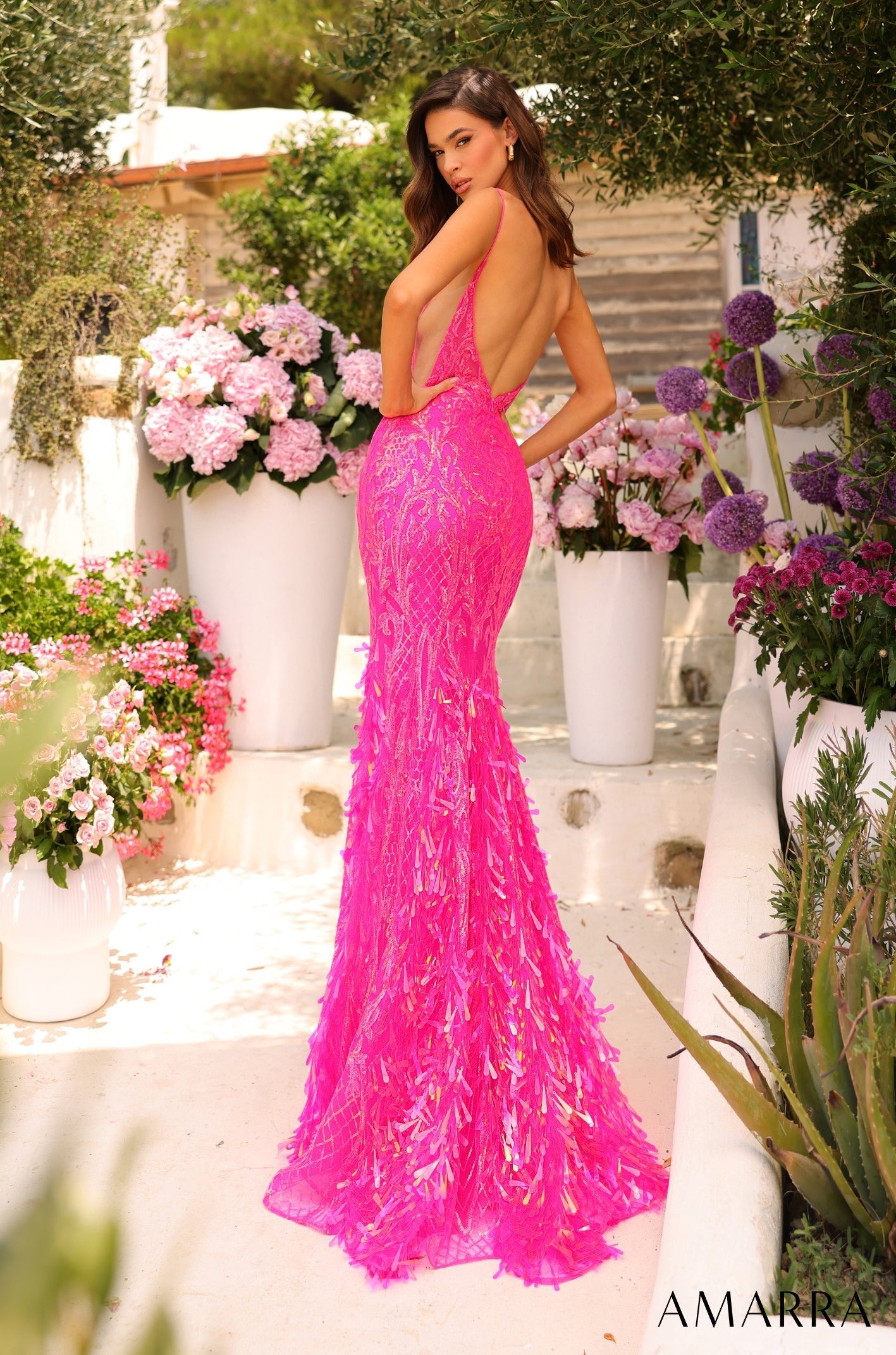 A vibrant hot pink sequined mermaid gown with a low back, photographed in a garden with white flowers.