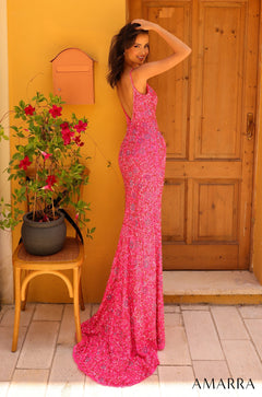 A woman in a sparkling pink floor-length gown poses by a wooden door with red flowers.