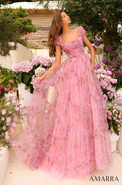 A woman in a voluminous pink floral gown stands gracefully among pink and purple flowers in a garden.