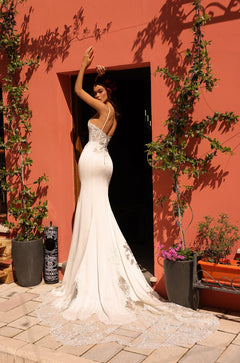 A bride in a white lace mermaid wedding dress poses by a coral wall with climbing vines.