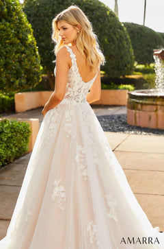 A blonde woman wears a white lace wedding gown with floral appliqués in a garden setting.