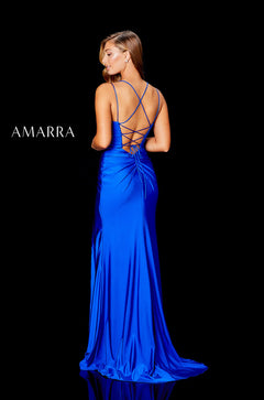 A woman in a blue floor-length gown with a lace-up back, standing against a black background.
