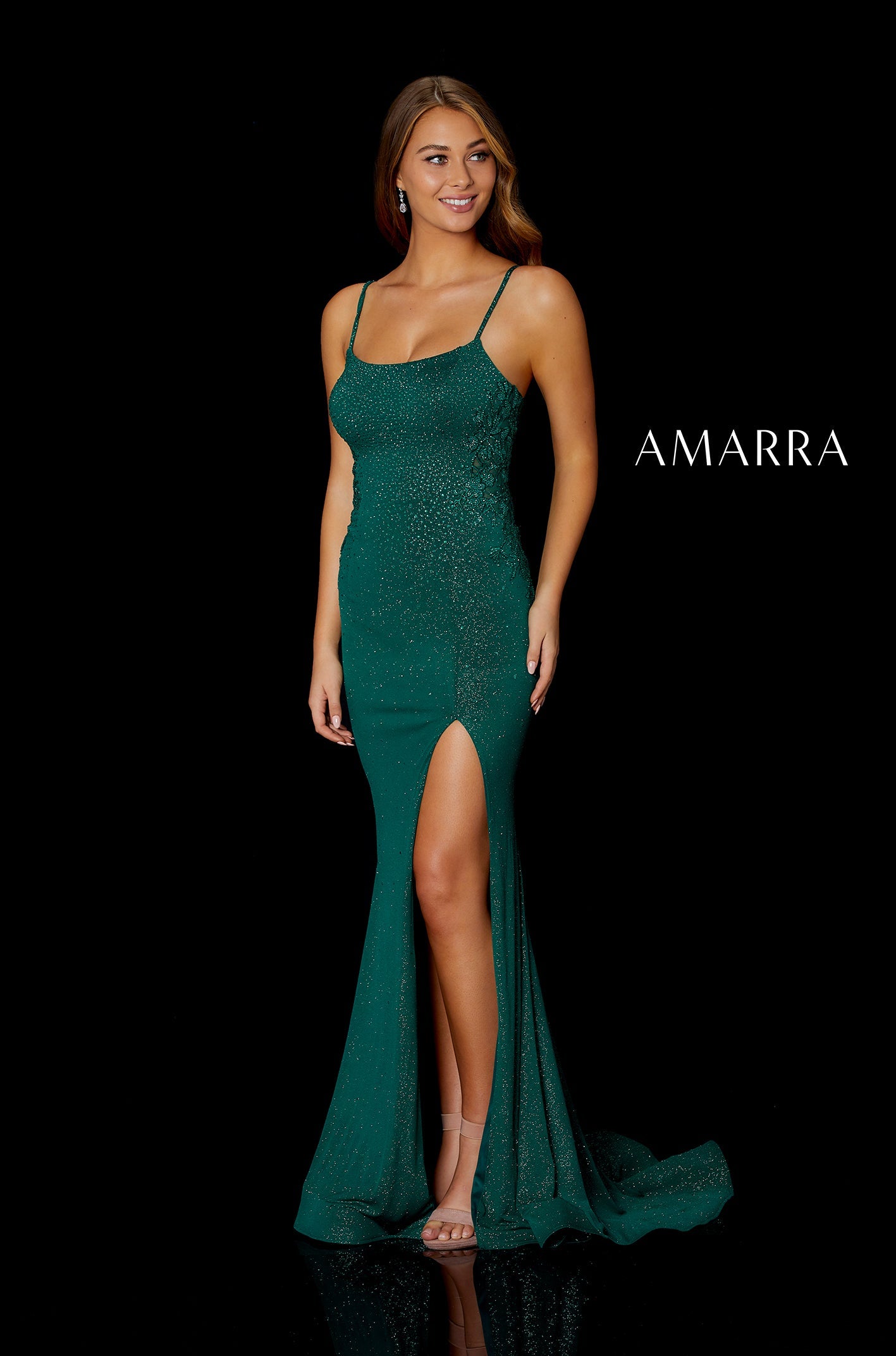 A woman in a shimmering emerald green gown with a high slit poses against a black background.