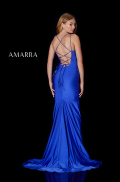 A woman wears a long, royal blue, shimmering gown with a criss-cross back, posing against a black background.