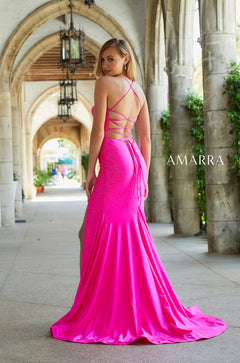 A model wears a bright pink floor-length gown with a strappy back and side slit in an arched stone corridor.
