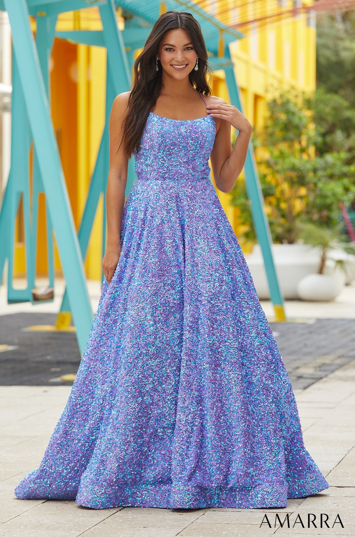 A woman wears a sparkling blue and purple sequined ball gown against a teal and yellow background.