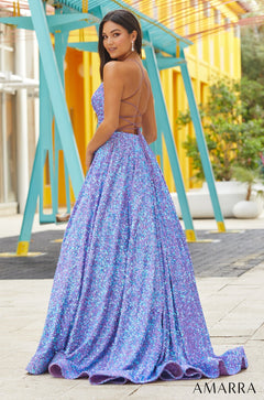 A woman in a floor-length, iridescent blue-purple sequin gown with a strappy back poses in an outdoor setting.