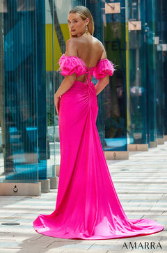 A long hot pink off-shoulder gown with feathered sleeves and a dramatic train against a glass building backdrop.