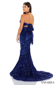 A woman wears a deep blue sequined mermaid-style evening gown with a halter neckline and long train.