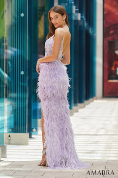 A woman wears a lavender feathered gown with a low back, posing against a modern glass backdrop.