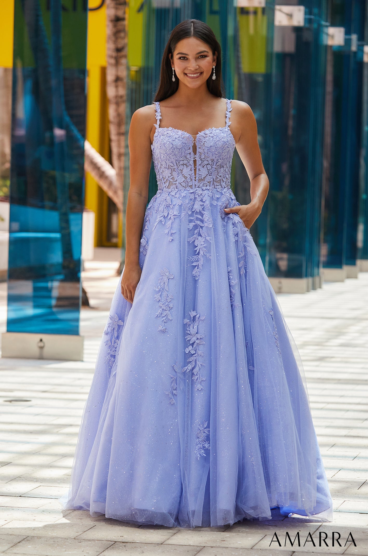 A woman wears a long periwinkle ballgown with floral appliqués and a sweetheart neckline.