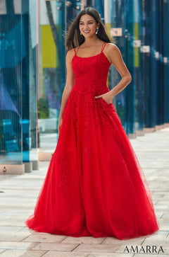 A woman in a red lace ballgown with spaghetti straps poses confidently against a blue-toned urban backdrop.