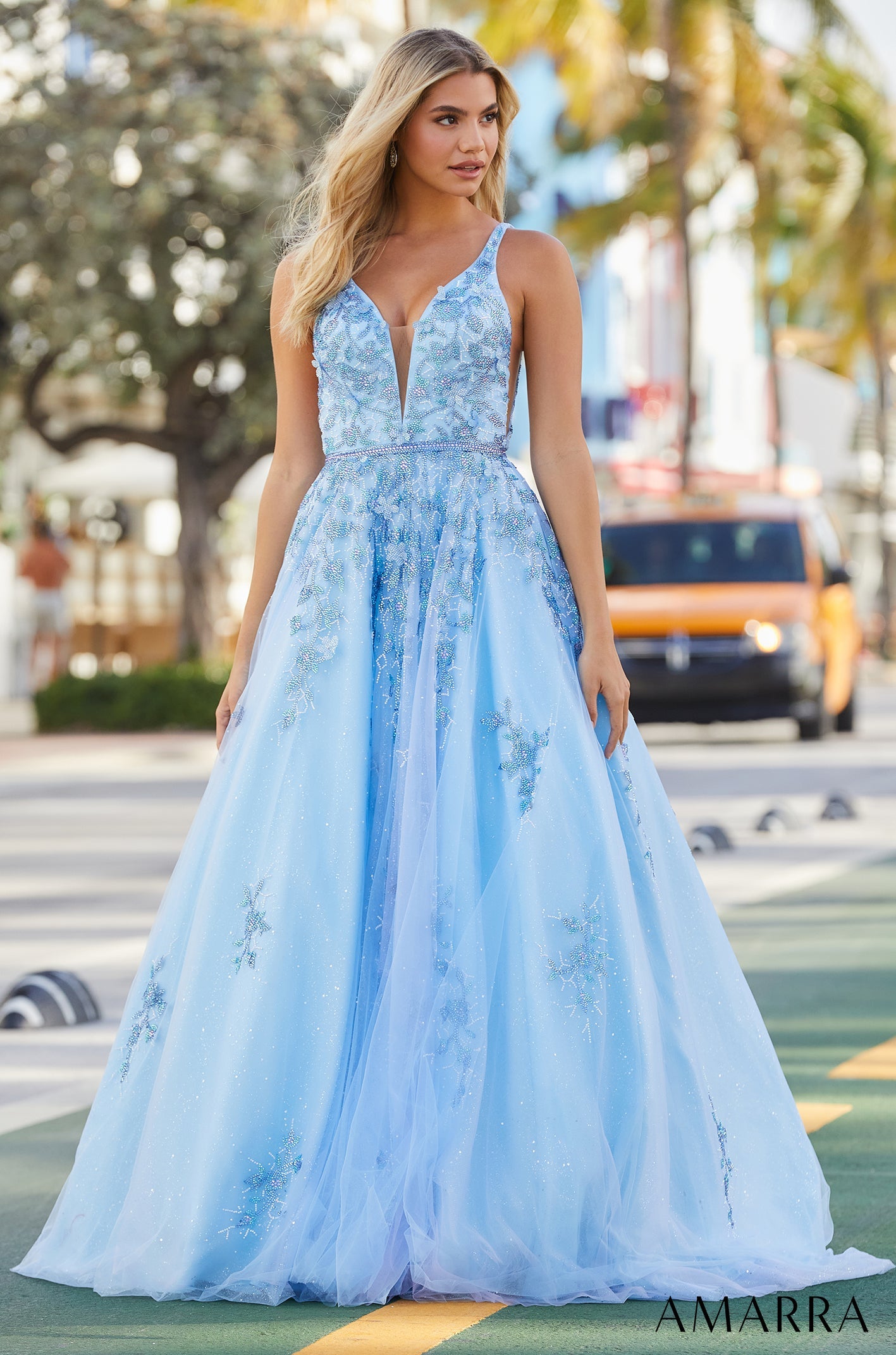 A pale blue ballgown with delicate floral embroidery and a deep V-neckline, worn on a city street.