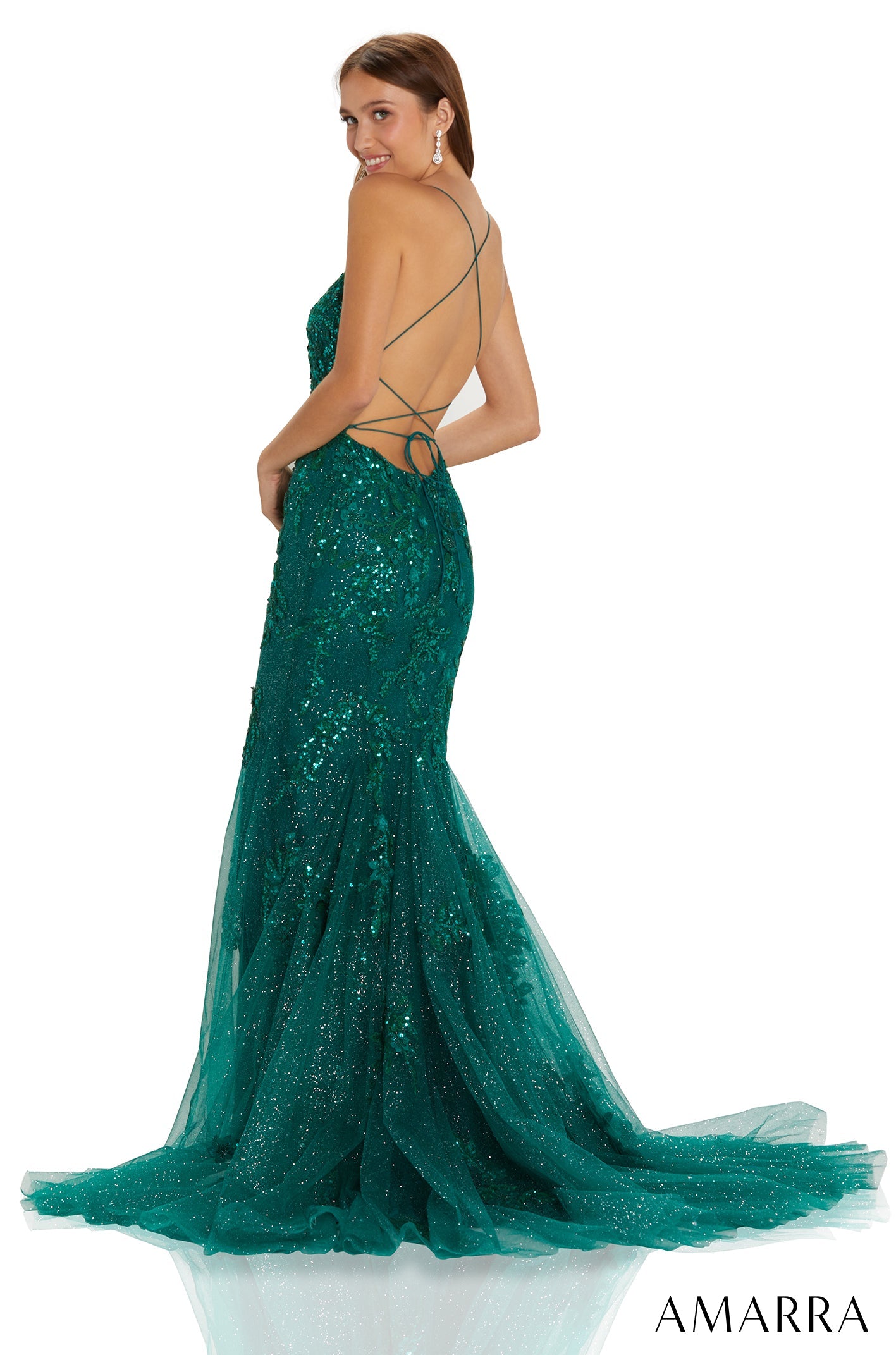 A woman in a shimmering emerald green mermaid gown with a low back, posing at an angle.