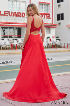 A model wears a long red evening gown with a lace back, standing in front of a hotel.
