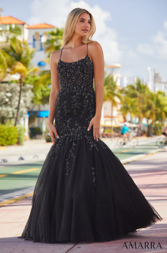 A blonde woman wears a black sequined mermaid gown with thin straps against a tropical street backdrop.