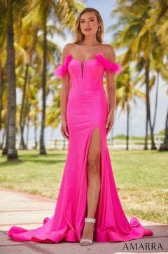 A woman wears a bright pink off-shoulder gown with feathered trim and a high slit, standing among palm trees.