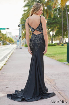 A long black sparkly evening gown with cut-out back stands on a palm-lined street with flowing train.