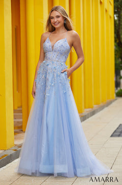 A light blue tulle A-line gown with floral embellishments and spaghetti straps stands against a yellow background.
