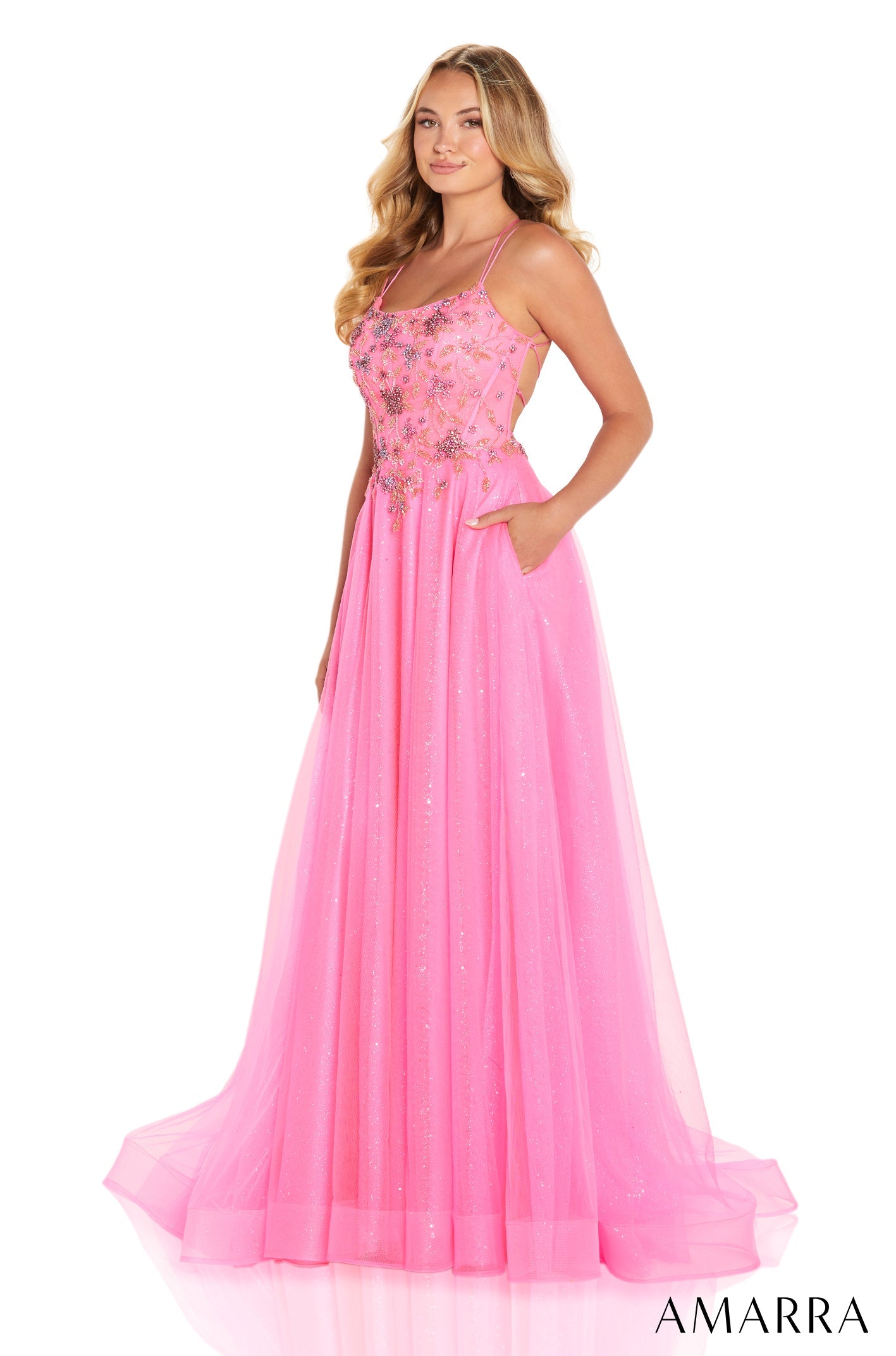 A woman wears a long, sparkly pink tulle gown with spaghetti straps and an embellished bodice.