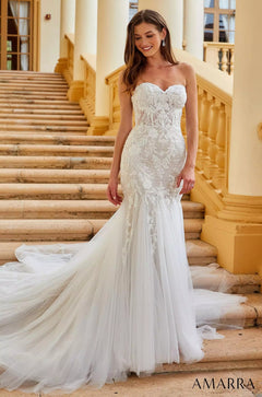 A bride in a strapless lace mermaid wedding gown stands on marble stairs in an elegant, sunlit setting.