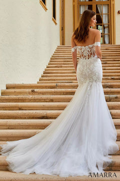 A bride in an off-shoulder lace mermaid wedding gown stands on stone steps.