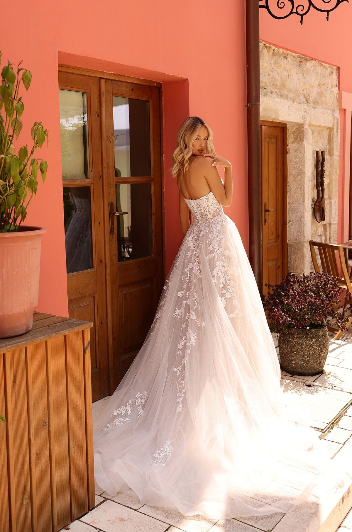 A bride in a white lace ballgown poses near wooden doors with a long, floral-embroidered train.